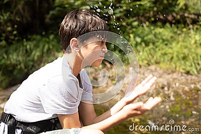 Funny, fresh little thirsty, cute brunette screwed up boy washing face with splash of water from river in nature, forest Stock Photo