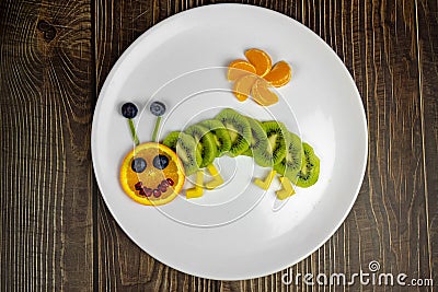 Funny fruit worm on white plate healthy dessert for kids on wooden table Stock Photo