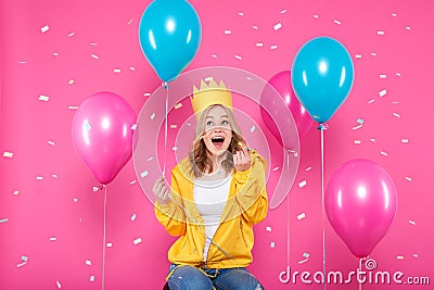 Funny girl in birthday hat, balloons and flying confetti on pastel pink background. Attractive teenager celebrating birthday. Stock Photo