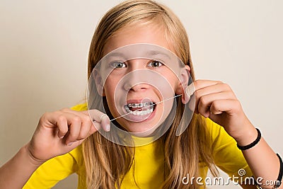 Funny girl with dental braces flossing her teeth. Close-up portrait of pre teen girl with dental floss isolated. Stock Photo