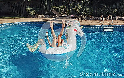 Funny girl dropped fell from inflatable ring unicorn. Kid child enjoying having fun in a swimming pool. Summer outdoor water Stock Photo