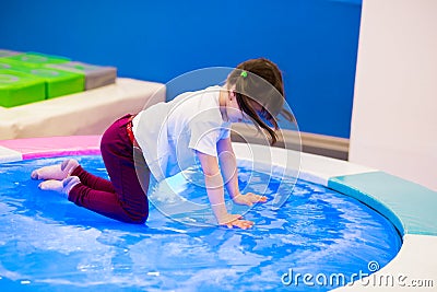 Funny girl preschooler with ponytails in a white T-shirt plays, jumps on an inflatable water trampoline with backlight. Stock Photo