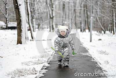 A funny girl in a warm silver jumpsuit runs along the path in winter. Stock Photo