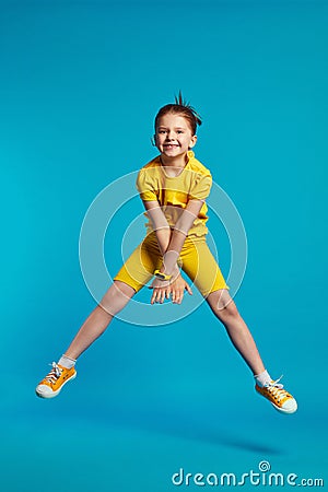 Funny girl wears yellow sportswear jumping on a colored blue background Stock Photo
