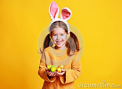 Funny happy child girl with easter eggs and bunny ears on yellow Stock Photo