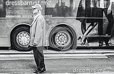 Funny image of a senior man seen on a city road next to a travel coach which is advertising clothing. Editorial Stock Photo