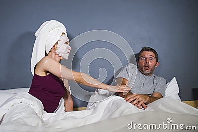 Funny lifestyle portrait of man and woman featuring weird married couple with wife in head towel and makeup face mask demanding se Stock Photo