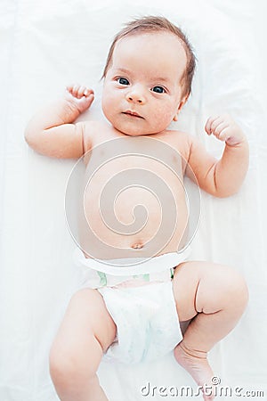 Funny little baby wearing a diaper lying on a white sheet. Child after bath or shower. Infant nappy change and skin care Stock Photo