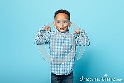 Funny little black boy showing biceps and smiling at camera, male child demonstrating his power and strength Stock Photo