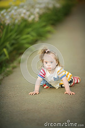 Funny little girl with Down syndrome creeps along the path Stock Photo