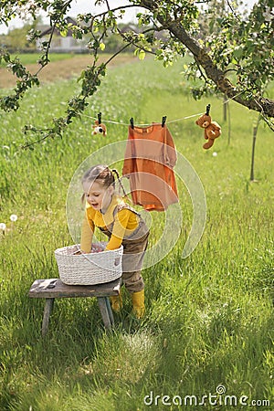 A funny little girl dressed in a rustic style takes clean washed wet underwear out of the basket Stock Photo