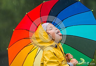 Funny little girl playing in the garden under the autumn rain. Kid wearing yellow waterproof coat and boots holding Stock Photo