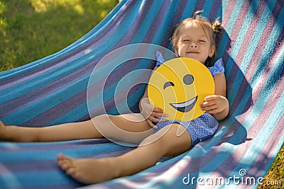 Girl is resting in hammock in nature holding a winking smile face in her hand Stock Photo