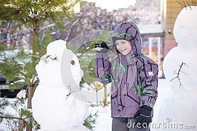 Funny little kid boy making a snowman and eating carrot, playing having fun with snow, outdoors on cold day. Active leisure childr Stock Photo