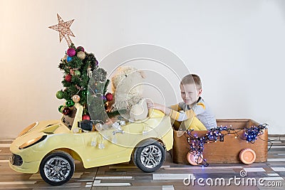 Funny little smiling kids driving toy car with Christmas tree. Happy child in colour fashion clothes bringing hewed xmas tree from Stock Photo