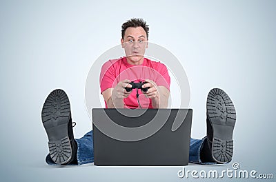 Funny man gamer sitting on the floor playing on laptop Stock Photo
