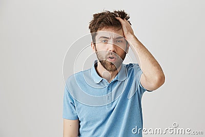 Funny mature bearded man with messy hair and beard, rubbing head and being tired or having hangover, standing over gray Stock Photo