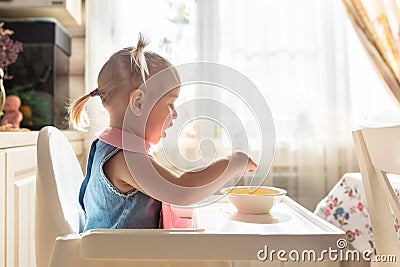 Funny naughty baby eating alone in the high chair Stock Photo