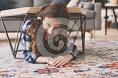 Funny naughty kid girl hiding under coffee table at home. Child playing Stock Photo