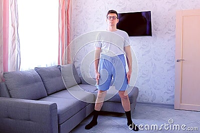 Funny nerd man is doing fitness exercises pelvis rotations at home. Sport humor concept. Stock Photo