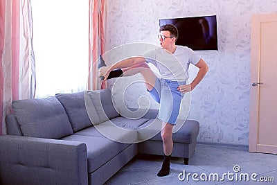 Funny nerd man is doing forward slopes and stretching exercises for legs at home. Sport humor concept. Stock Photo