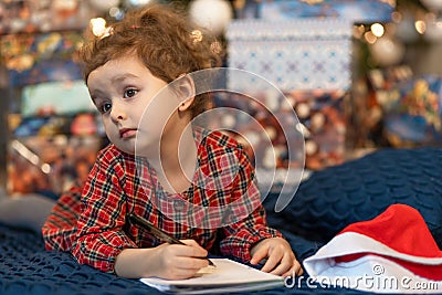 Pensive little girl writing letter to santa. kid making a wish, gift, present on new year eve. child dreaming under the christmas Stock Photo