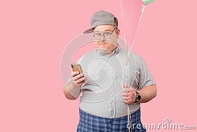 Funny plump guy standing with phone and balloons having doubts isoated on pink Stock Photo