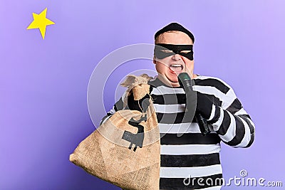 Funny plump thief with a sack holding a torch and using it like microphone Stock Photo