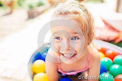 Portrait of adorable blonde happy liitle girl close-up. Girl is in a pool with multicolor baloons. Summertime Stock Photo