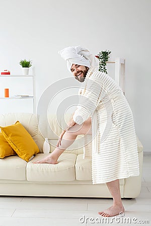 Funny portrait of handsome beautiful guy in towel and bathrobe holding tube of body cream lotion in hand. Spa, body and Stock Photo