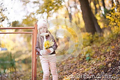 Funny portrait of a little girl. Little girl in a pink hat on a walk in the fall. Child girl in a jacket happily runs and collects Stock Photo