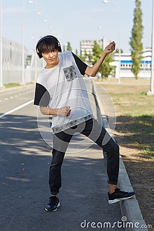 Funny, positive, handsome asian guy dancing in headphones on a street background. Teenage years concept. Stock Photo