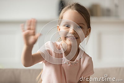 Little preschooler girl sit on couch waving looking at camera Stock Photo