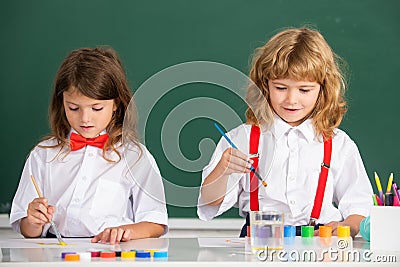 Funny pupils draws in classroom. School friends kids boy and girl painting together in class on school blackboard Stock Photo