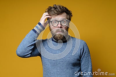 Funny, puzzled man tries to remember something, gathers thoughts, clings to his head with hand and looks bewildered. Stock Photo