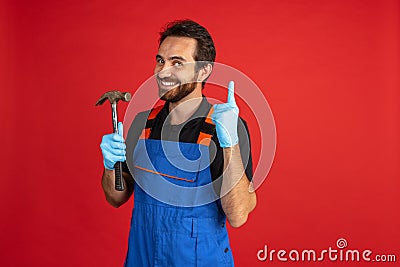 Funny young bearded man, male auto mechanic or fitter wearing blue work dungarees isolated over red studio background Stock Photo