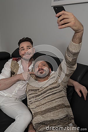 Funny romantic male gay couple using smartphone for video call. Family time in the living room Stock Photo