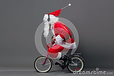 Funny Santa Claus with a long white beard in sunglasses and headphones rides a bicycle on the white background. Stock Photo