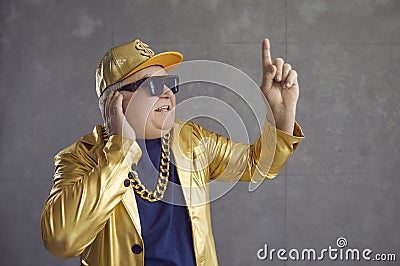 Funny senior DJ in golden jacket, baseball cap and chain necklace mixing music at disco party Stock Photo