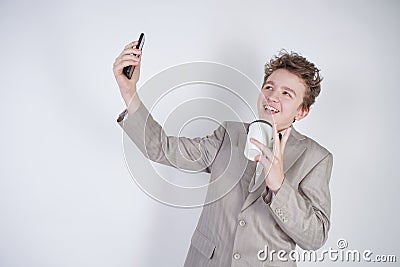 Funny smiling teenager having fun with smartphone in his hands. teen boy wearing grey business suit standing with paper cup of cof Stock Photo