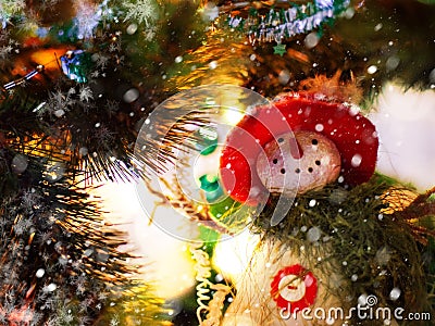 Funny snowman in a red hat and green scarf on the background of Christmas tree branches with lights Stock Photo