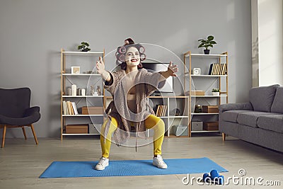 Funny tired housewife in face mask and curlers squatting during sports workout at home Stock Photo