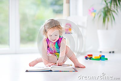 Funny toddler girl reading a book sitting on a fllor Stock Photo