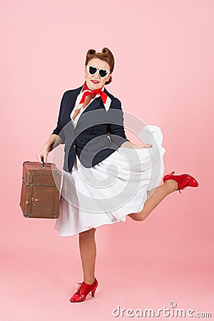 Funny traveler girl with suitcase and black sunglasses. Brunette woman in pin-up style with vintage case. Stock Photo