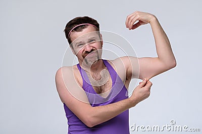 Funny weak sportsman exercising looking on his biceps Stock Photo