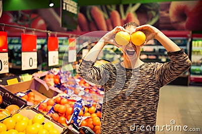 Funny woman holding grapefruit for her eyes.Young woman shopping for recipe ingredients in a supermarket having fun at the grocery Stock Photo