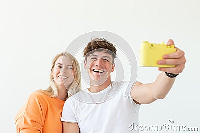 Funny young couple in love cute man and charming woman making selfie on vintage yellow film camera posing on a white Stock Photo