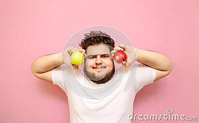 Funny young man in white t-shirt and overweight isolated on pink background with 2 apples in hands on pink background. Fat Stock Photo