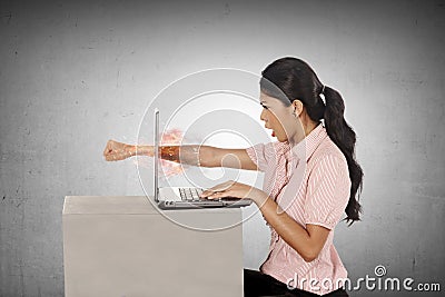 Furious asian business woman throws a punch into the laptop Stock Photo