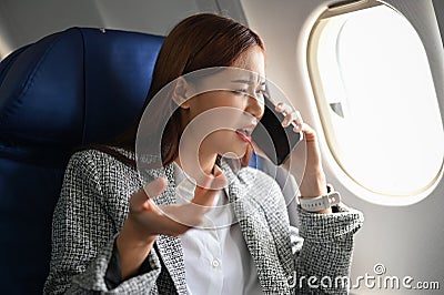 Furious asian businesswoman having a serious talk on the phone during the business flight Stock Photo